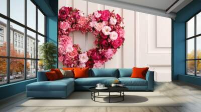 A heart-shaped wreath made of various pink and red flowers, hanging on a white wooden door. Wall mural