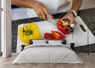 Woman with red manicure cutting red and yellow peppers on a chopping board Wall mural