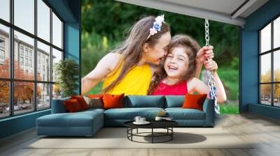 Two happy beautiful girls sitting on seesaw and smiling at warm summer day Wall mural