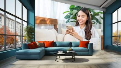 Asian beautiful girl using mobile phone, sitting in the living room. Wall mural