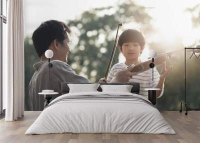 Asian father give and teach young boy kid to play violin in park together. Man educate music skill to his child to be specialist and professional in future. Nature outdoor violin class in evening. Wall mural