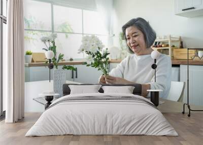 Asian senior old woman puts flowers on vase with happiness in kitchen. Wall mural