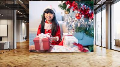 Asian young happy girl kid wear Santa hat and decorate Christmas tree.  Wall mural