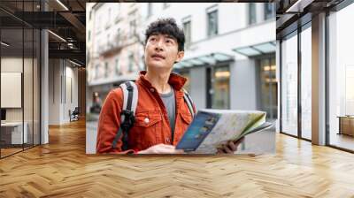 Asian young man backpacker traveler looking at map to find destination.  Wall mural