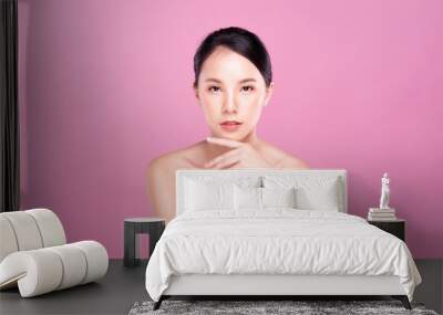 Beautiful Young Asian woman with clean fresh white skin touching her own face softly in beauty pose. Girl touching with fingers in pink background. Facial treatment, cosmetology, spa, make up concept. Wall mural