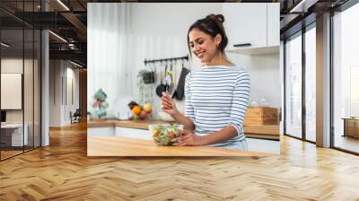 Caucasian young woman eating healthy green salad in kitchen at home.  Wall mural