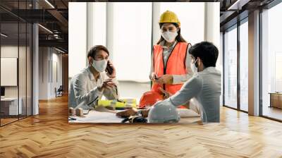 Group of building architect construction engineer have meeting and brainstorm together on table discussing about new project, teamwork talk with colleague. Members wear face mask prevent covid19 virus Wall mural