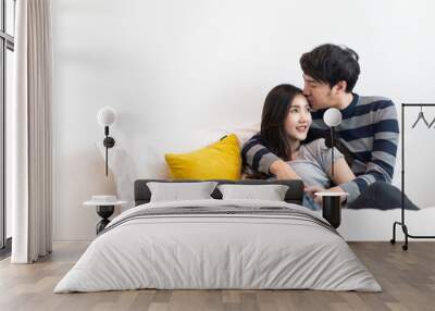 Lovely Asian couple sitting on bed in bedroom together. Boy holding girl head softly and be hand in hand or pinky swear to love girl. Man kissing woman on smile young lady cheek feeling shy & happy. Wall mural