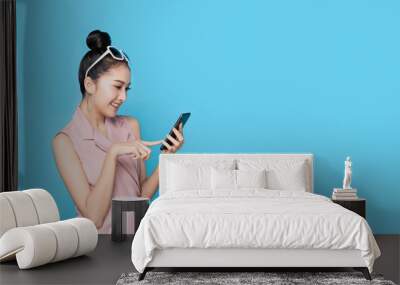 Portrait of Asian beautiful young woman holding smartphone and pointing finger on mobile phone with smile face. The girl standing and looking at phone in studio. Advertisement & presentation concept. Wall mural