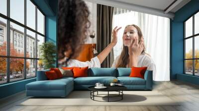 Two young beautiful woman putting smooth facial mask on face in bedroom.  Wall mural