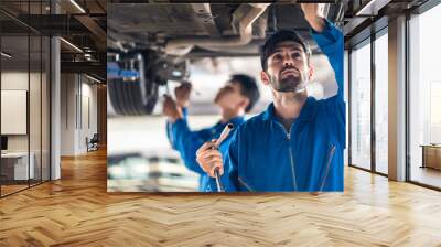 Vehicle service maintenance handsome mens checking under car condition on lifter in garage. Automotive mechanic man use tool to tighten and replace damaged or broken part. Car repair service concept. Wall mural