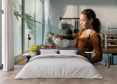 Young beautiful Latino woman pouring clean water into glass in kitchen Wall mural