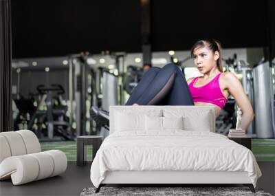 Young fit muscle Asian woman exercising and working out in gym. Pretty girl in sportswear sit up on the floor, looking in front of her focus on training building abs muscular, abdominal strength. Wall mural