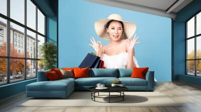 Young pretty cute Asian Caucasian woman holding shopping bags with smiley face standing in studio, okay posture fingers. Girl wearing hat and dress in summer style costume. Happy shopping summer sale. Wall mural