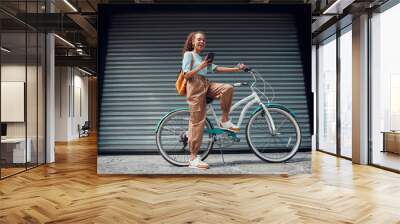 Bicycle, woman and phone in city feeling excited and happy about message while outdoor in summer with trendy look. Eco friendly transportation for carbon footprint female on a bike using 5g network Wall mural