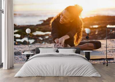 My body thanks me for each yoga practice. Shot of an attractive young woman sitting on a mat and stretching while doing yoga on the beach at sunset. Wall mural