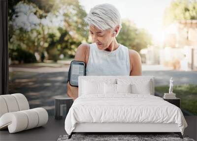 Senior woman, fitness and phone armband listening to music for morning run in an urban street outdoors. Active elderly female runner checking smartphone to monitor training exercise or navigation Wall mural