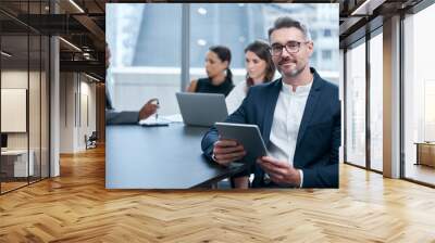 Were always busy making big things happen here. Portrait of a mature businessman using a digital tablet in an office with his colleagues in the background. Wall mural