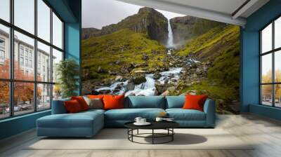 Cold water in Iceland. Waterfall in rocky mountains. Fresh and green grass. Beautiful mountain range in the backgrond. Wall mural