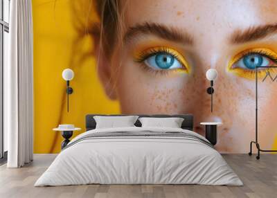 close-up of a girl with yellow eye shadow and blue eyes on a yellow background Wall mural