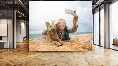 A young woman is photographed with a dog on the beach, they laugh and are amused. Wall mural