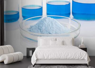 Blue biological powder in a petri dish in the foreground. In the background are laboratory flasks with blue liquid. Wall mural