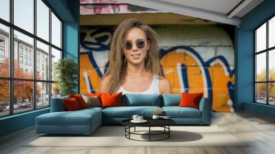 Portrait of young beautiful woman wearing white tank shirt and blue jeans on brick wall with graffiti background Wall mural