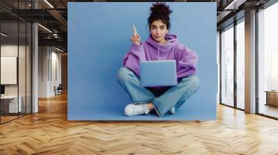 Full body photo girl sit floor legs crossed work laptop point index finger copyspace direct way follow comment ads wear lilac violet pullover denim jeans isolated blue color background Wall mural