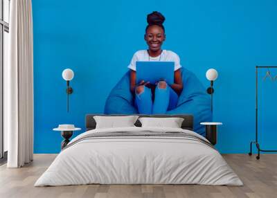 Full body young smiling student fun happy black woman in casual clothes shirt white t-shirt sit in bag chair hold use work on laptop pc computer isolated on plain dark blue background studio portrait. Wall mural