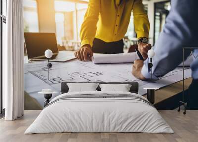 two business partners in formal wear and with protective yellow helmets on heads walking and talking about business younger one holding folder with data while older one using tablet Wall mural