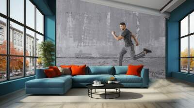 Athlete doing sprint hiit high intensity interval training. Male fitness model in fashion sportswear in city. Runner sprinting on urban gray background. Sport, workout, healthy lifestyle concept. Wall mural