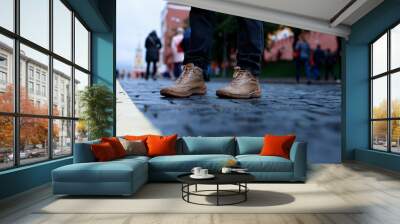 Boots on man legs with black jeans in stone pavement in perspective. Old street paved with stone blocks with yellow line in the middle. Shallow depth of field. Wall mural