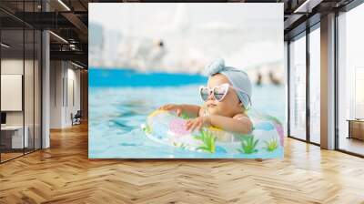 Cute funny toddler girl in colorful swimsuit and sunglasses relaxing on inflatable toy ring floating in pool have fun during summer vacation in tropical resort. Child having fun in swimming pool.  Wall mural