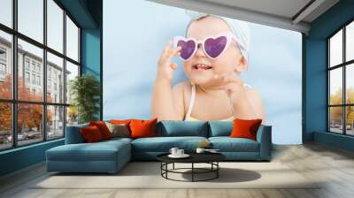 Funny cute baby girl on summer vacation. Child having fun in swimming pool. Sweet toddler girl in colorful swimsuit and sunglasses relaxing on sunbed. Free space for text. Wall mural