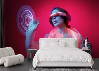 Woman in futuristic costume. Girl in glasses of virtual reality while touching air. Augmented reality game, future technology, AI concept. VR. Neon red light. Viva magenta color of the year 2023.  Wall mural