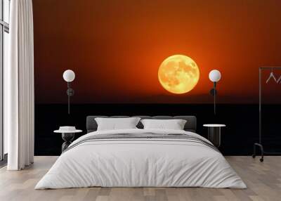 A full moon rising over a dark ocean at sunset, with an orange and red sky in the background Wall mural