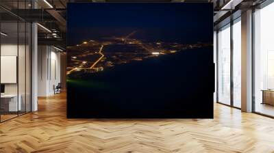 Aerial view of a coastal city at night, with a winding road and scattered lights illuminating the landscape against a dark background Wall mural