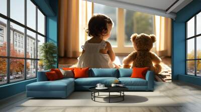 Charming baby with teddy bear sitting on rug, basking in warm morning light by the window Wall mural