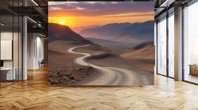 Scenic winding dirt road meandering through a vast mountainous desert landscape illuminated by a vibrant sunset Wall mural