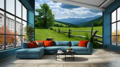 Tranquil countryside vista featuring a tree stump and rustic wooden fence with lush hills and majestic mountains beneath a dramatic cloudy sky Wall mural