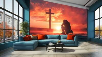 A man kneels and prays in front of a cross. Wall mural