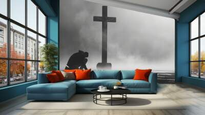 A man kneels and prays in front of a cross. Wall mural