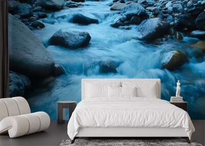 Serene Blue Mountain Stream: Long exposure of tranquil water cascading over rocks in a scenic riverbed with a calming blue and white color scheme. Wall mural