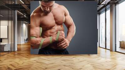 closeup of bodybuilder holding tape measure. wrong biceps measuring concept. muscular young man trie Wall mural