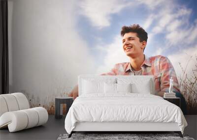 handsome young man sitting and smiling on sky background. attractive caucasian teenage boy wearing s Wall mural