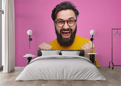 Happy bearded man wearing glasses standing with fists up on pink background. Epic win concept Wall mural