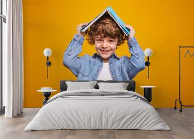 Happy schoolboy hiding under textbook Wall mural