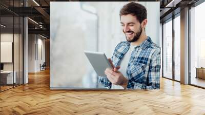 Smiling man playing on digital tablet Wall mural