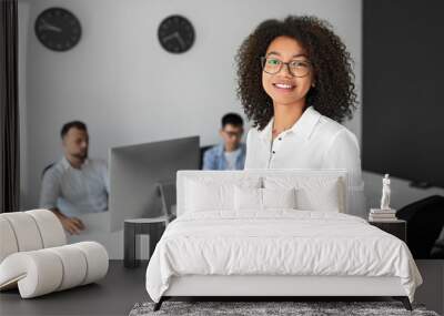 Smiling woman looking at camera in office with colleagues Wall mural