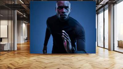 Young black athlete running against blue background Wall mural